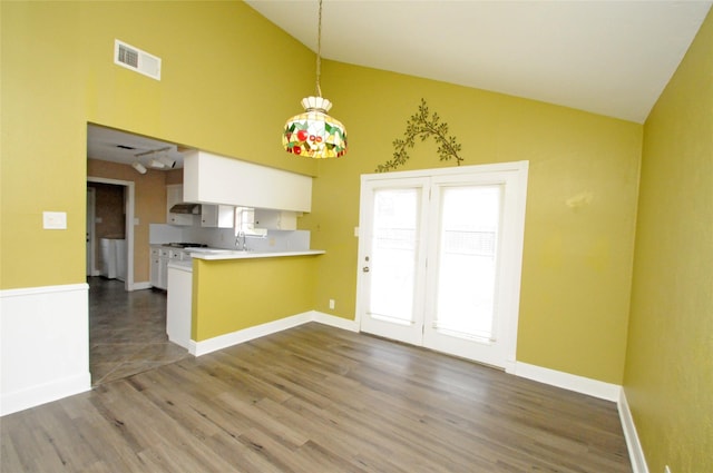 kitchen with wood finished floors, light countertops, visible vents, a peninsula, and high vaulted ceiling