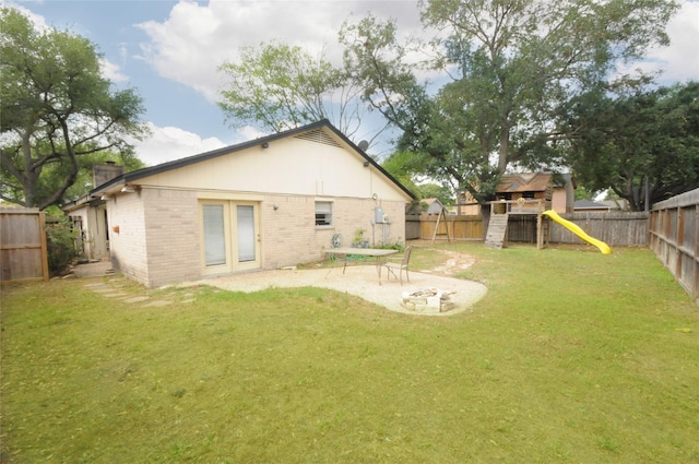 rear view of house featuring a playground, a chimney, a lawn, brick siding, and a fenced backyard
