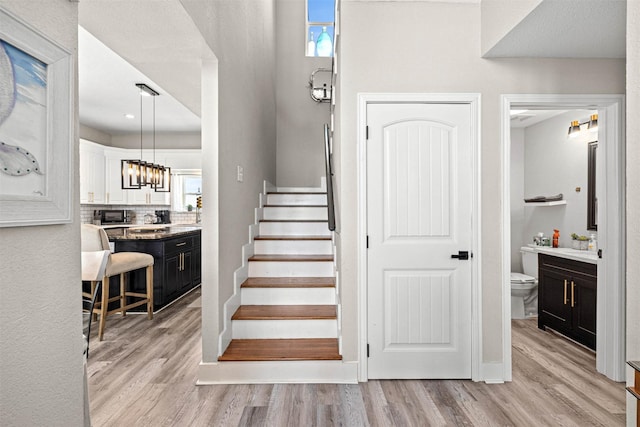 stairs featuring an inviting chandelier, wood finished floors, and a healthy amount of sunlight