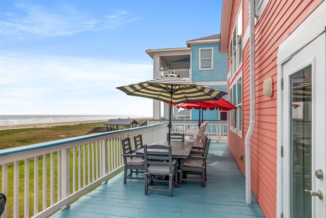 deck featuring a beach view, outdoor dining area, and a water view