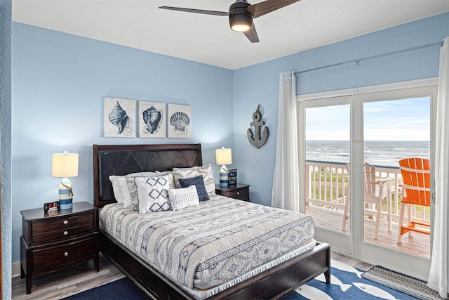bedroom with a water view, access to outside, a ceiling fan, and wood finished floors