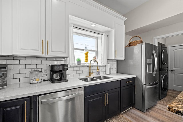 kitchen featuring white cabinetry, stacked washer / dryer, appliances with stainless steel finishes, light wood finished floors, and a sink