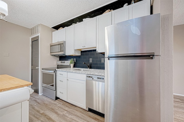 kitchen featuring light wood-style floors, light countertops, a sink, stainless steel appliances, and decorative backsplash