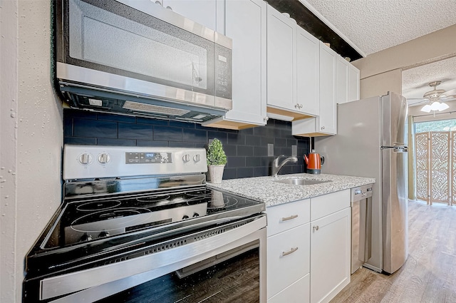 kitchen with a textured ceiling, white cabinetry, stainless steel appliances, light wood finished floors, and a sink