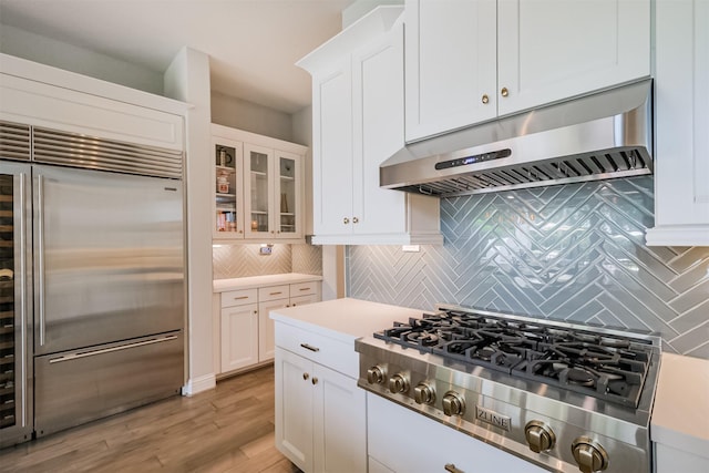 kitchen with light wood-style flooring, white cabinetry, light countertops, under cabinet range hood, and appliances with stainless steel finishes