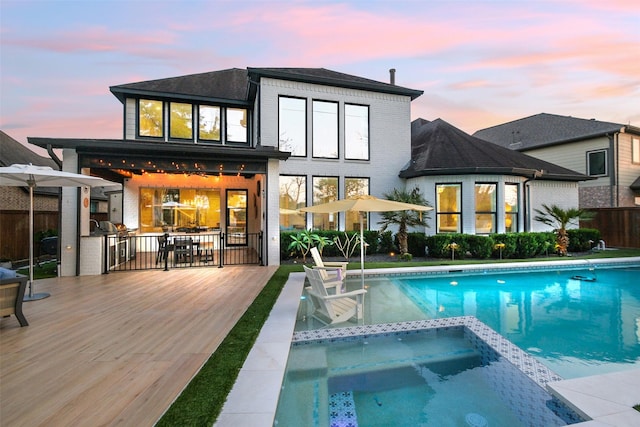 rear view of property with a wooden deck and a pool with connected hot tub