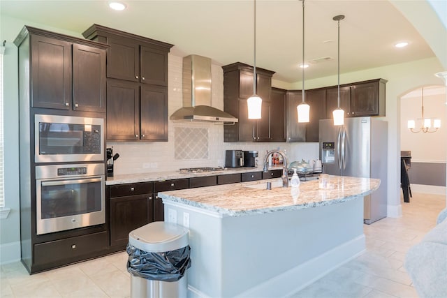 kitchen with a sink, dark brown cabinets, appliances with stainless steel finishes, and wall chimney range hood