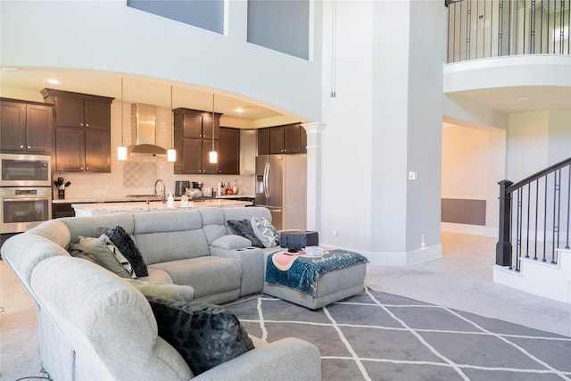 living room with arched walkways, light carpet, baseboards, stairway, and a high ceiling