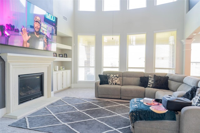 carpeted living area with built in shelves, a towering ceiling, visible vents, and a glass covered fireplace