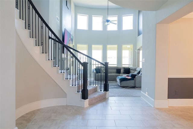 staircase featuring baseboards, visible vents, ceiling fan, and a high ceiling