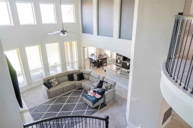 living room with a towering ceiling, a ceiling fan, baseboards, and carpet floors