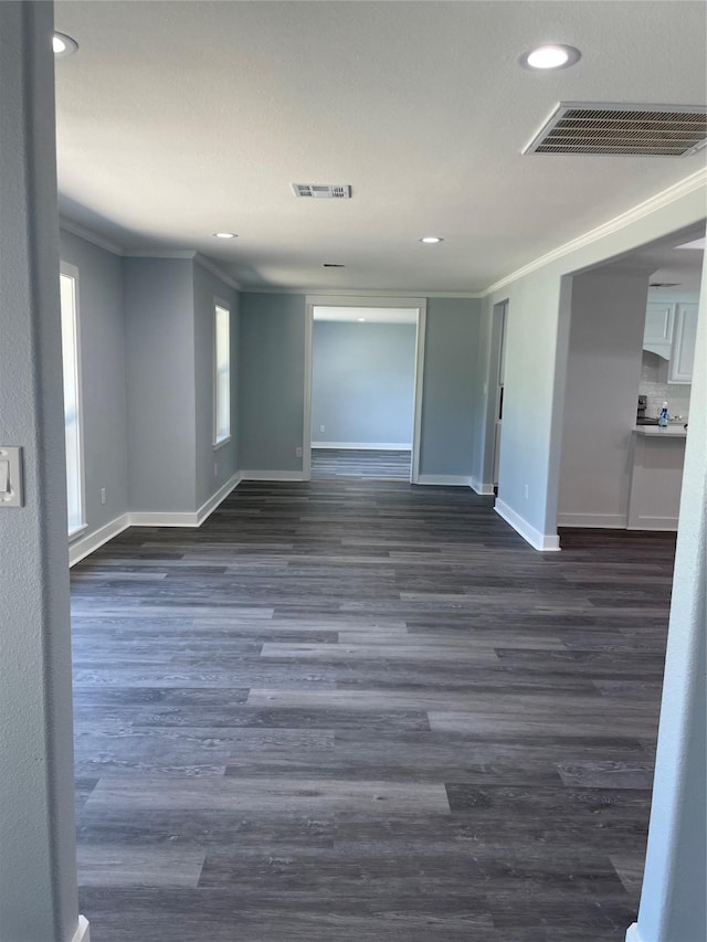 empty room with crown molding, visible vents, baseboards, and dark wood finished floors