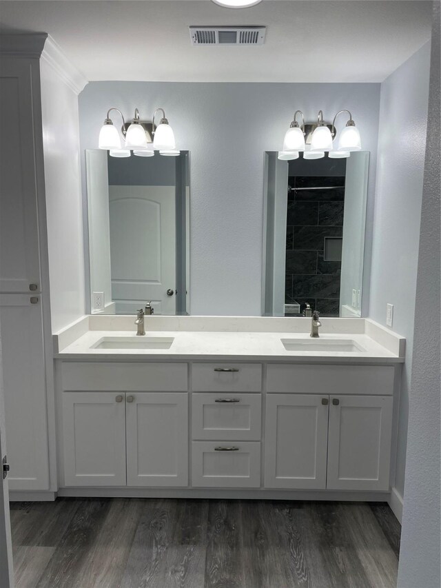 full bath with double vanity, visible vents, a sink, and wood finished floors