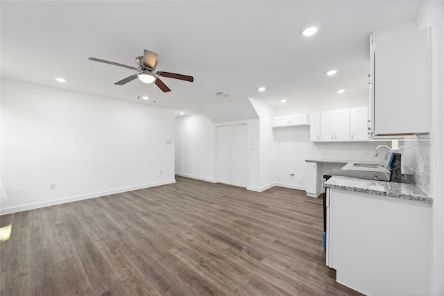 kitchen with ceiling fan, dark wood finished floors, light stone countertops, white cabinetry, and baseboards