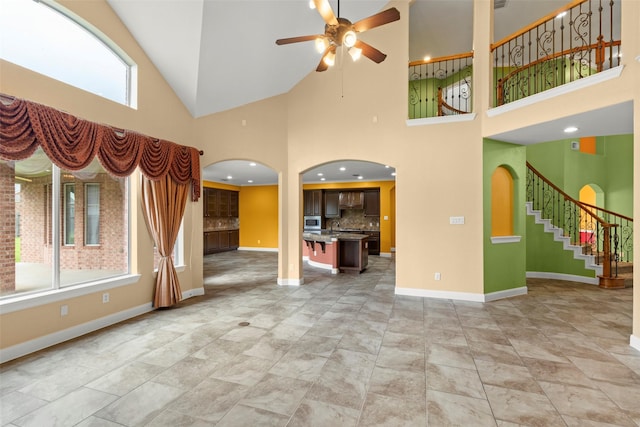 unfurnished living room featuring arched walkways, ceiling fan, baseboards, and stairway