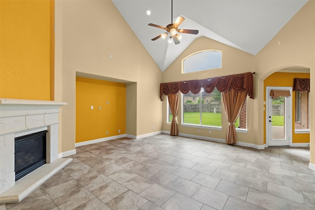 unfurnished living room with arched walkways, high vaulted ceiling, a glass covered fireplace, a ceiling fan, and baseboards