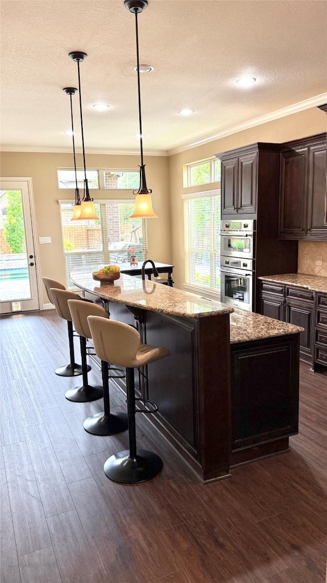 34315 E Short Leaf Pine Ct, Pinehurst, TX 77362 - kitchen with dark brown cabinets, a breakfast bar, ornamental molding, double oven, and an island with sink
