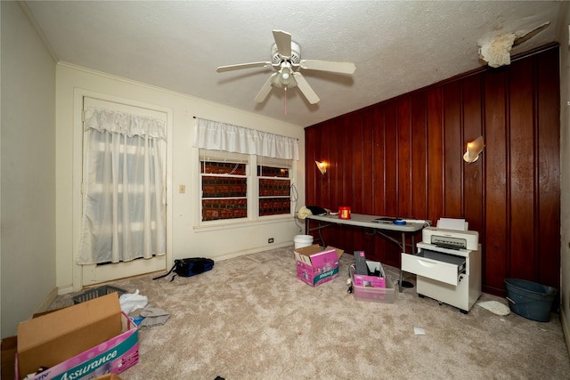 unfurnished office with crown molding, wooden walls, a ceiling fan, baseboards, and carpet floors