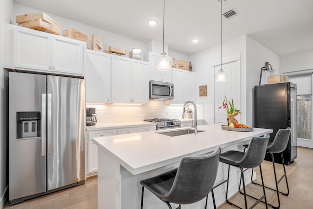 kitchen featuring a sink, decorative backsplash, light wood-type flooring, pendant lighting, and stainless steel appliances
