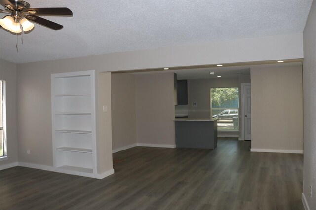 unfurnished living room featuring built in features, a textured ceiling, a ceiling fan, dark wood-style flooring, and baseboards