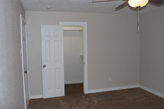 unfurnished bedroom with a walk in closet, a closet, a ceiling fan, and carpet
