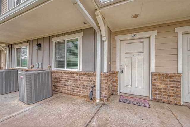 doorway to property featuring central AC, brick siding, and board and batten siding