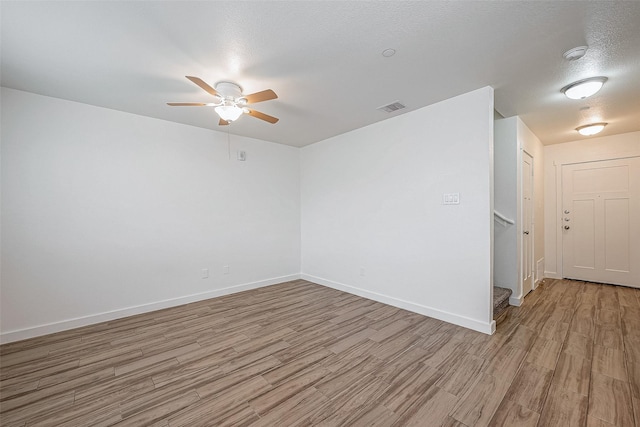 empty room with baseboards, stairway, visible vents, ceiling fan, and light wood finished floors