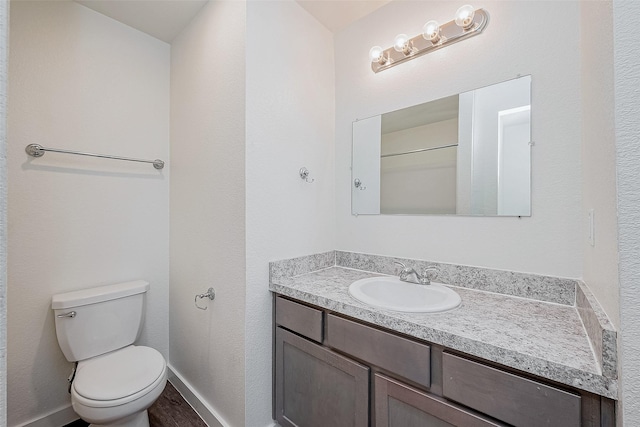 bathroom with toilet, wood finished floors, vanity, and baseboards