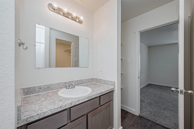 bathroom with a spacious closet, vanity, and wood finished floors