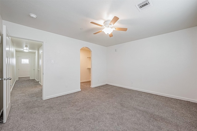carpeted spare room with visible vents, ceiling fan, arched walkways, and baseboards