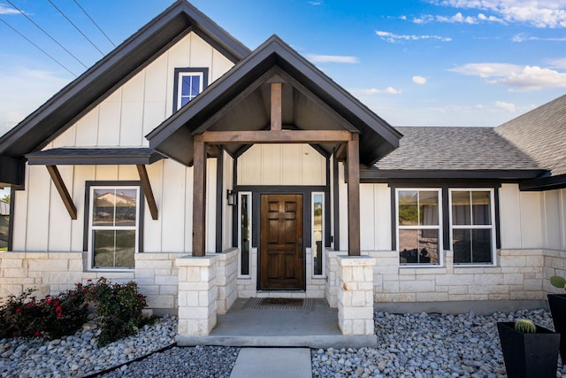 property entrance featuring roof with shingles, stone siding, and board and batten siding