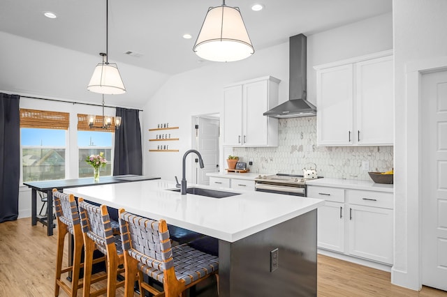 kitchen featuring tasteful backsplash, electric range, a center island with sink, wall chimney exhaust hood, and a sink