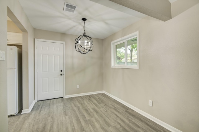 unfurnished dining area featuring a chandelier, wood finished floors, baseboards, and visible vents
