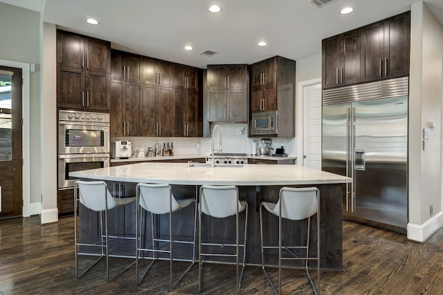 kitchen featuring dark wood-type flooring, built in appliances, baseboards, and dark brown cabinetry