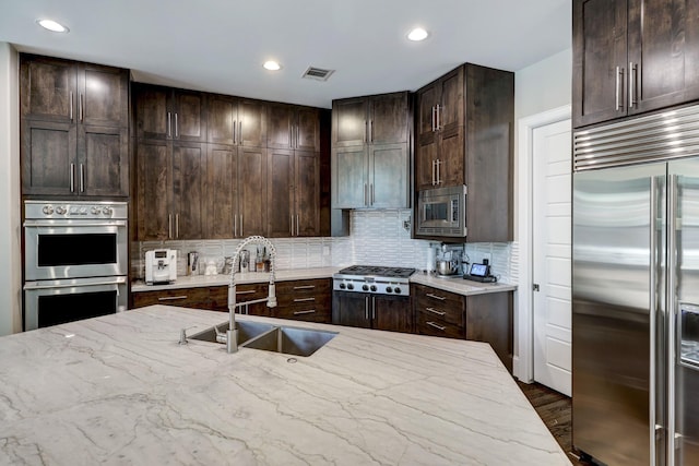 kitchen with a sink, dark brown cabinets, built in appliances, and light stone counters