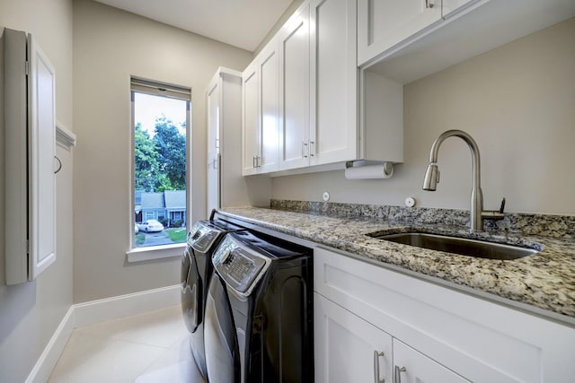 washroom with light tile patterned floors, baseboards, separate washer and dryer, a sink, and cabinet space