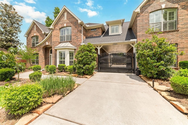 traditional home with concrete driveway, brick siding, a gate, and roof with shingles