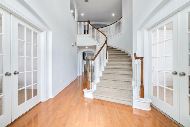 foyer entrance with arched walkways, french doors, stairs, wood finished floors, and a towering ceiling