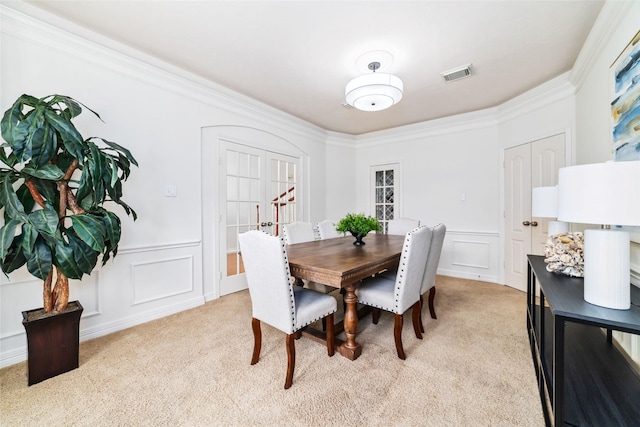 dining room with crown molding, light carpet, a decorative wall, and visible vents