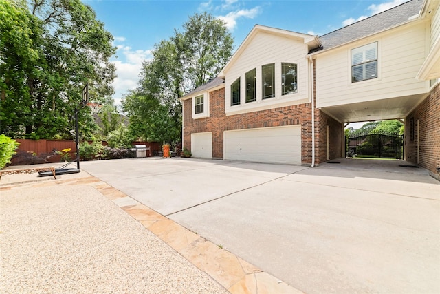 view of side of property featuring driveway, roof with shingles, a garage, brick siding, and fence
