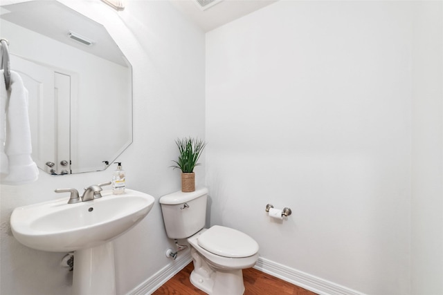 half bath with baseboards, wood finished floors, and toilet