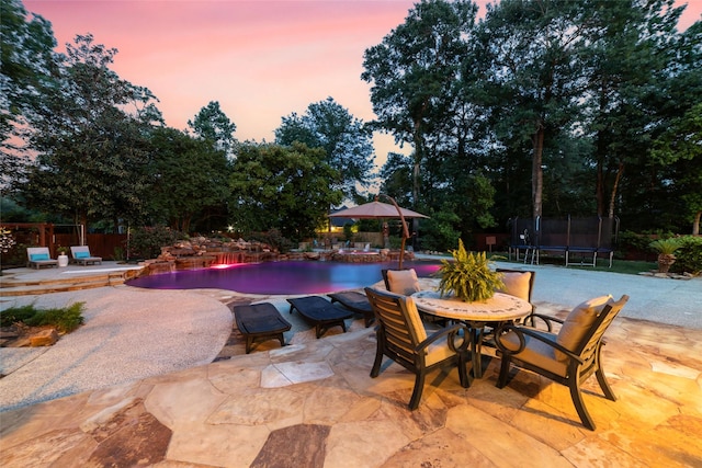 pool at dusk with fence, a patio, a trampoline, and an outdoor pool