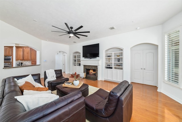 living area with a ceiling fan, visible vents, built in shelves, and light wood-type flooring