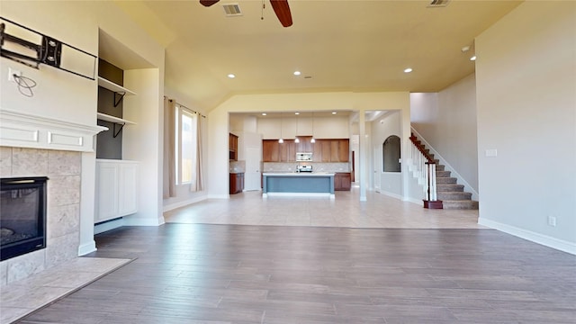 2135 Llerena Ln, League City, TX 77573 - unfurnished living room with ceiling fan, a tiled fireplace, baseboards, stairs, and light wood-style floors