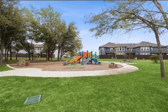 communal playground featuring a lawn, fence, and a residential view