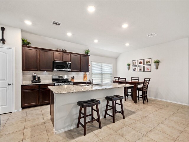 kitchen featuring stainless steel appliances, visible vents, dark brown cabinetry, and a kitchen bar