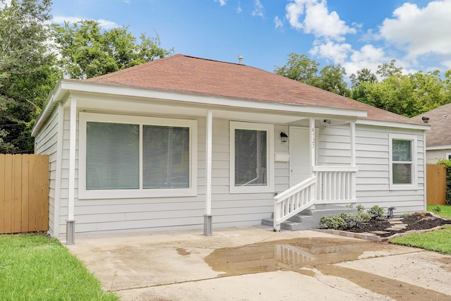 bungalow-style house with roof with shingles, fence, and a patio