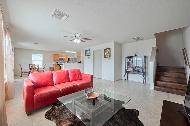 living room with visible vents, a ceiling fan, stairs, and light tile patterned floors