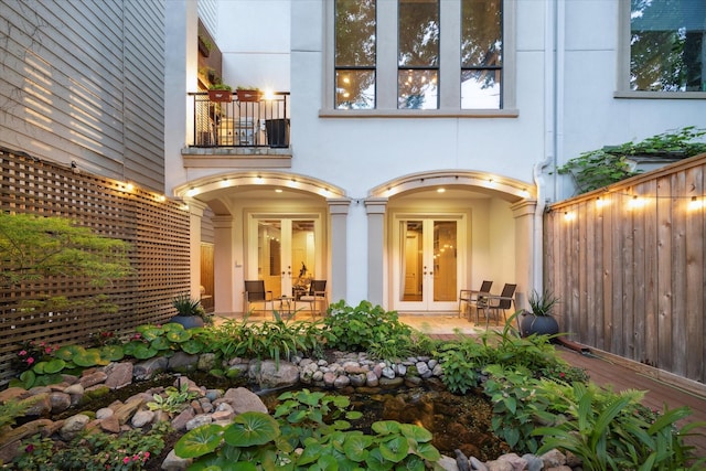 doorway to property with french doors, fence, stucco siding, and a balcony
