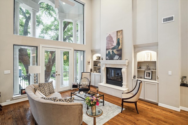 living area with a towering ceiling, a tiled fireplace, french doors, visible vents, and wood finished floors